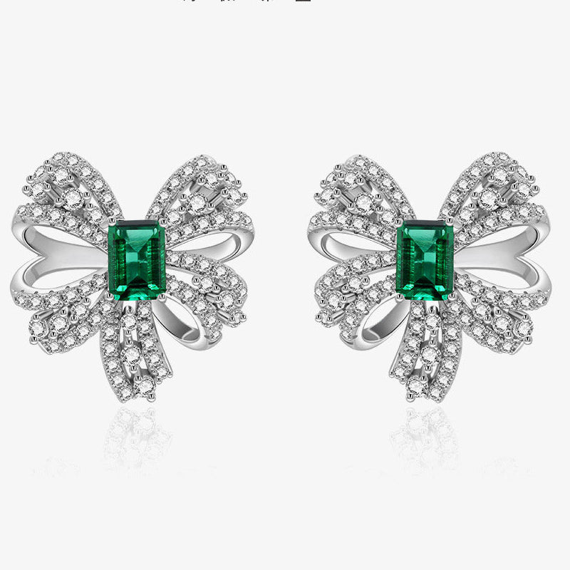 Bow-shaped earrings with green gemstones on a white background, featuring the SHIPEI JEWELRY brand.