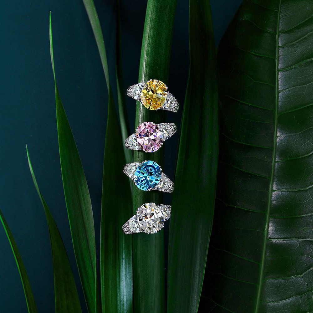 Five diamond rings with different colored gemstones on green leaves